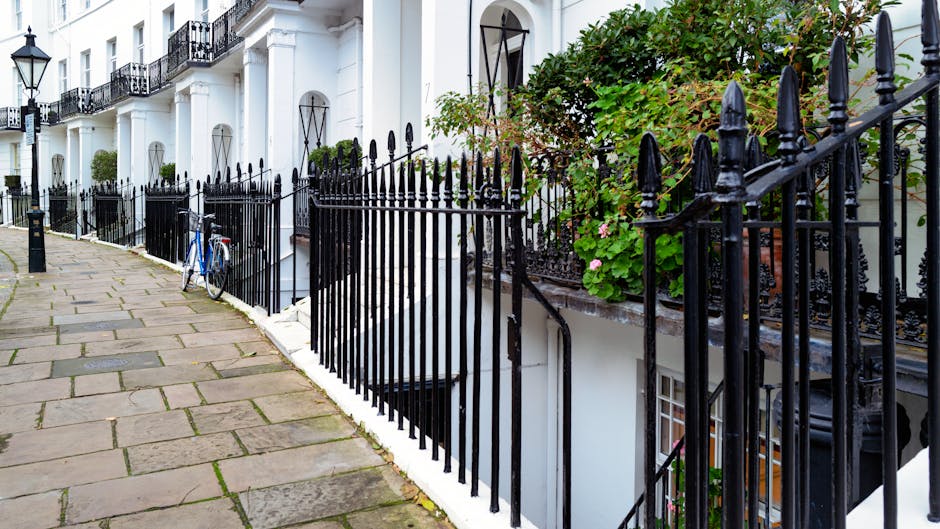 A row of white terraced houses with black wrought iron railings and decorative fencing along a paved sidewalk in Fleet Street terraces, Temple. The pavement consists of irregular stone slabs, some sho